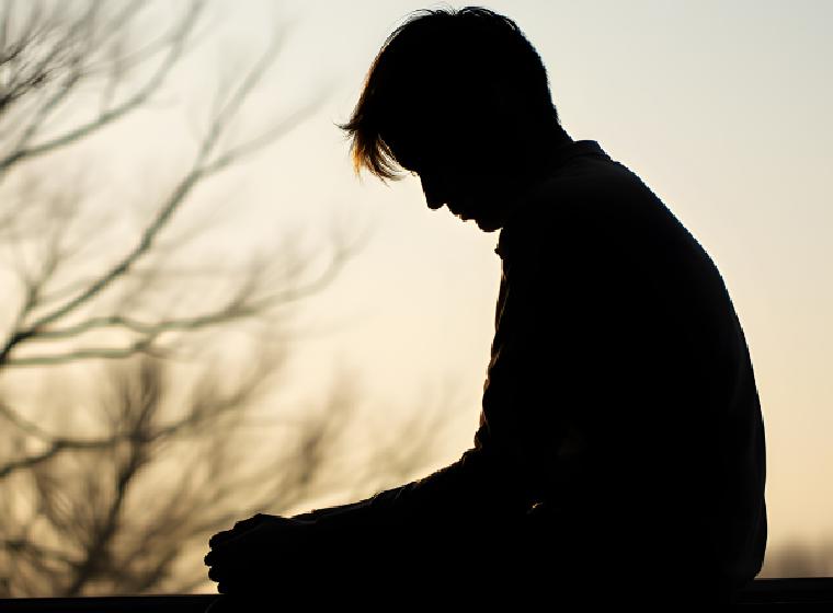 Silhouet van een jongeman die met gebogen hoofd zit