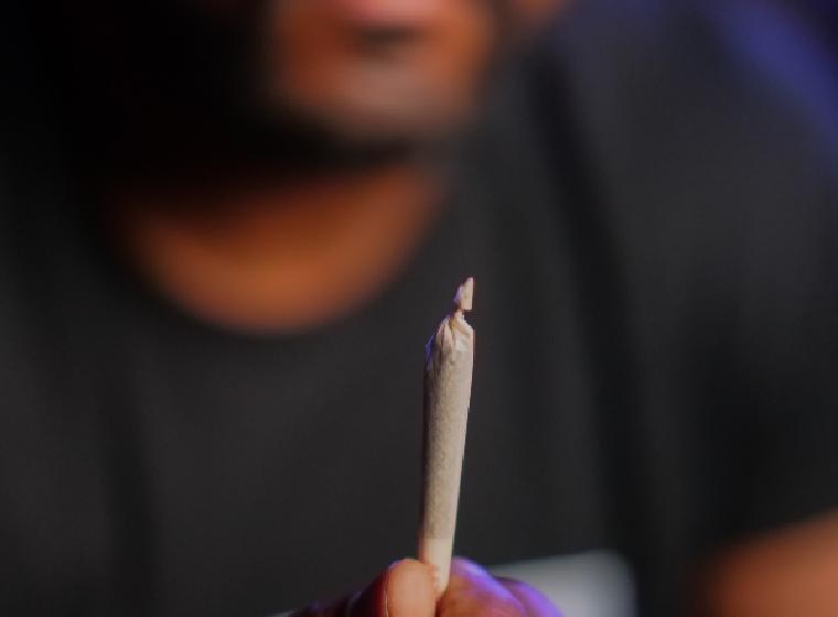 Man houdt een gedraaide joint tussen zijn vingers