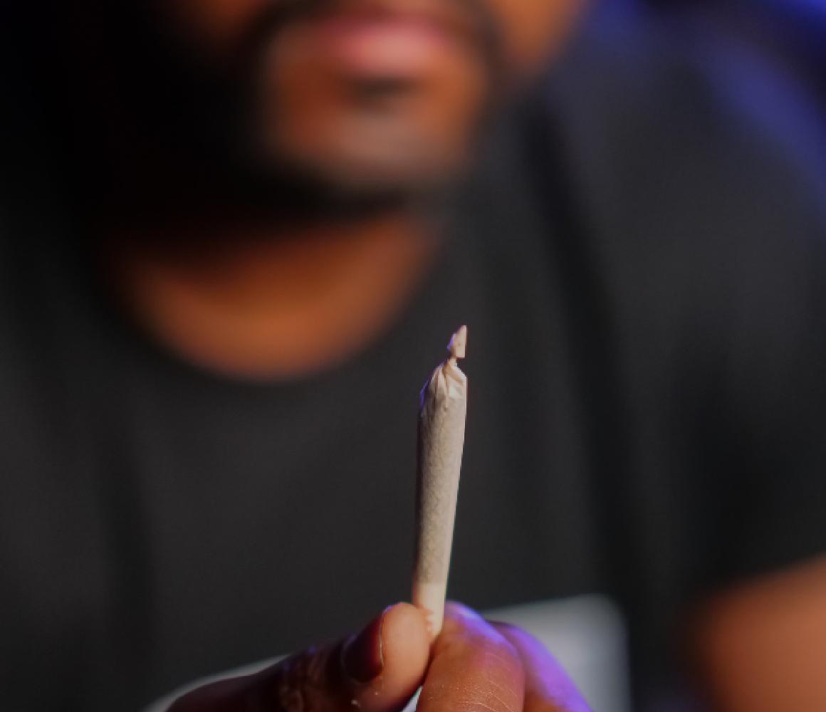 Man houdt een gedraaide joint tussen zijn vingers