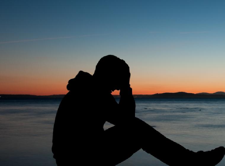 Silhouet van een man met het hoofd in zijn handen bij het water