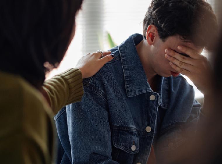 Iemand legt een hand op de schouder van een emotionele man