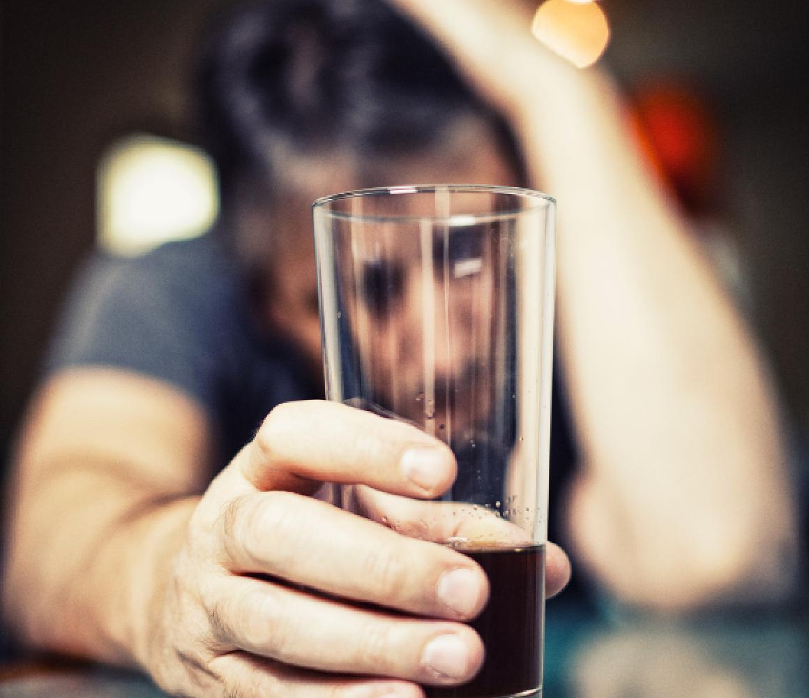 Man leunt vermoeid aan de bar met een glas drank in zijn hand