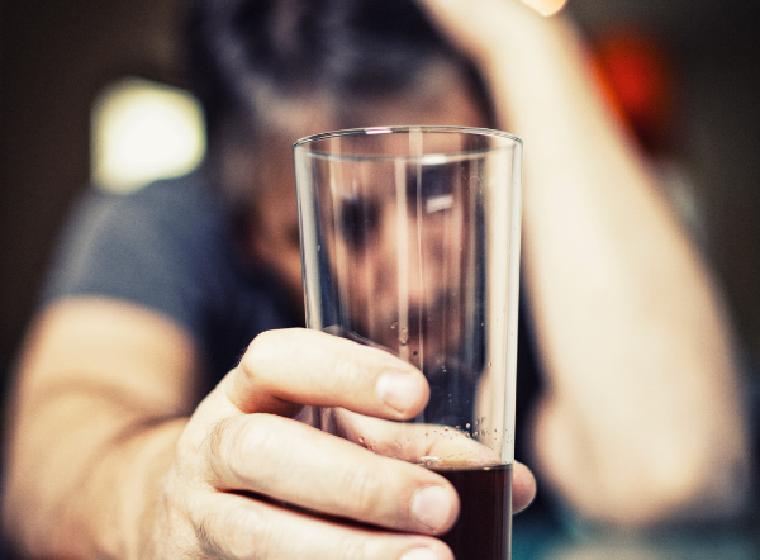 Man leunt vermoeid aan de bar met een glas drank in zijn hand
