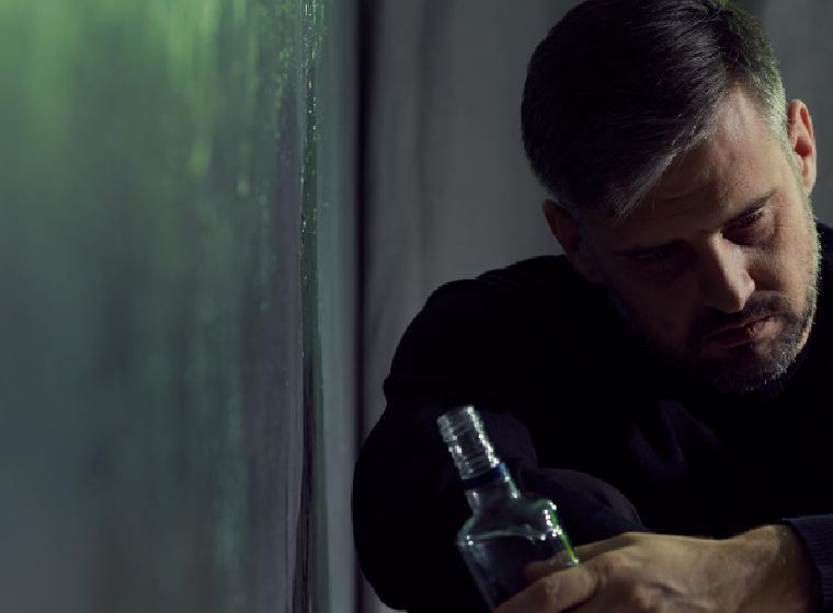 Man zit in schemerlicht met een fles in zijn handen