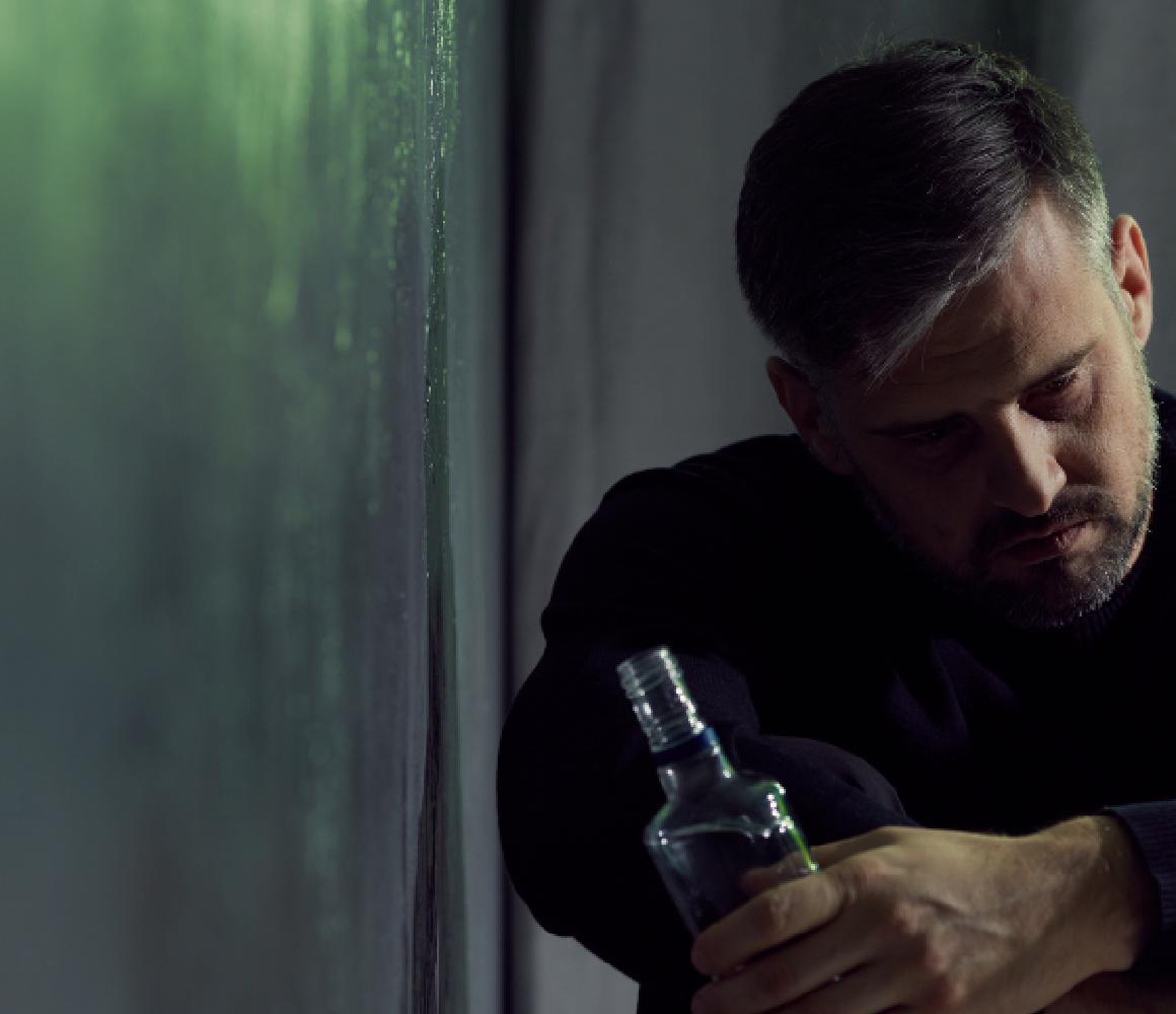 Man zit in schemerlicht met een fles in zijn handen