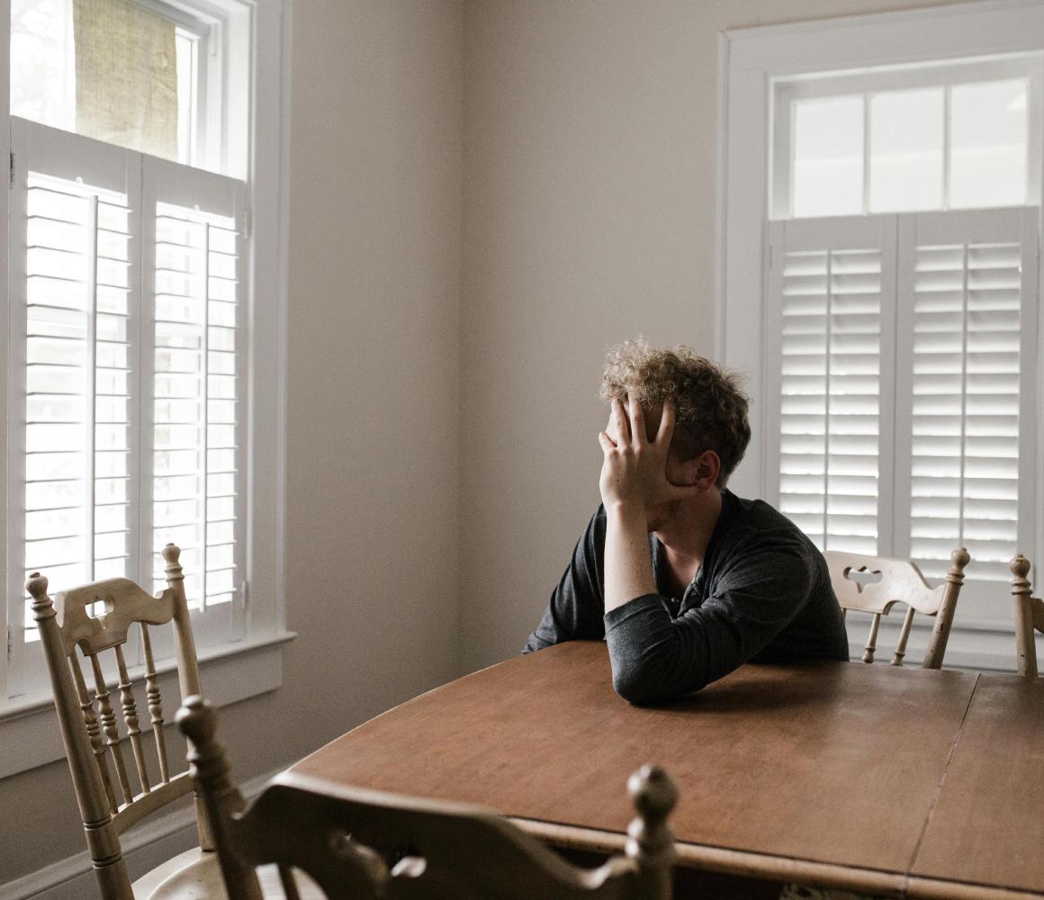 Man zit alleen aan een houten eettafel met het hoofd in zijn hand