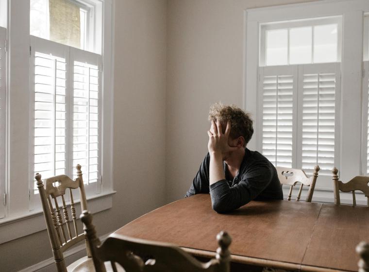 Man zit alleen aan een houten eettafel met het hoofd in zijn hand