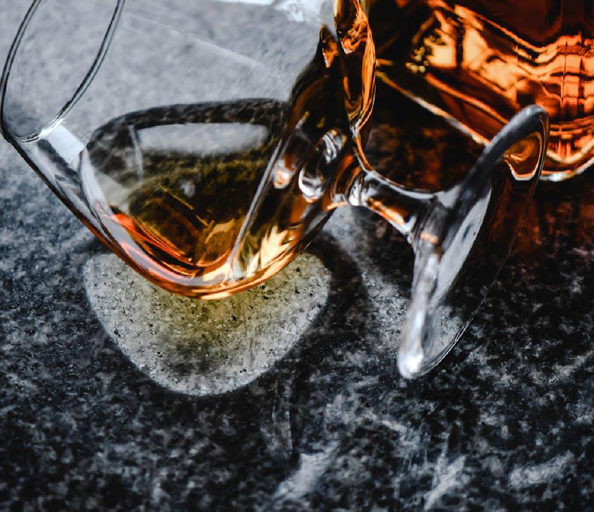 Omgevallen glas met amberkleurige drank op een marmeren tafel