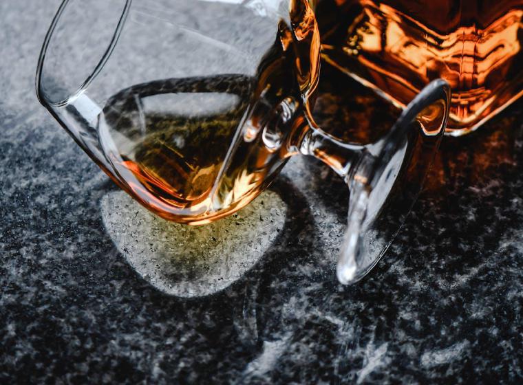 Omgevallen glas met amberkleurige drank op een marmeren tafel