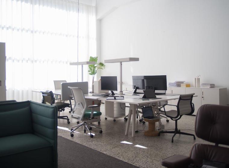 Leeg modern kantoor met bureaus, beeldschermen en bureaustoelen