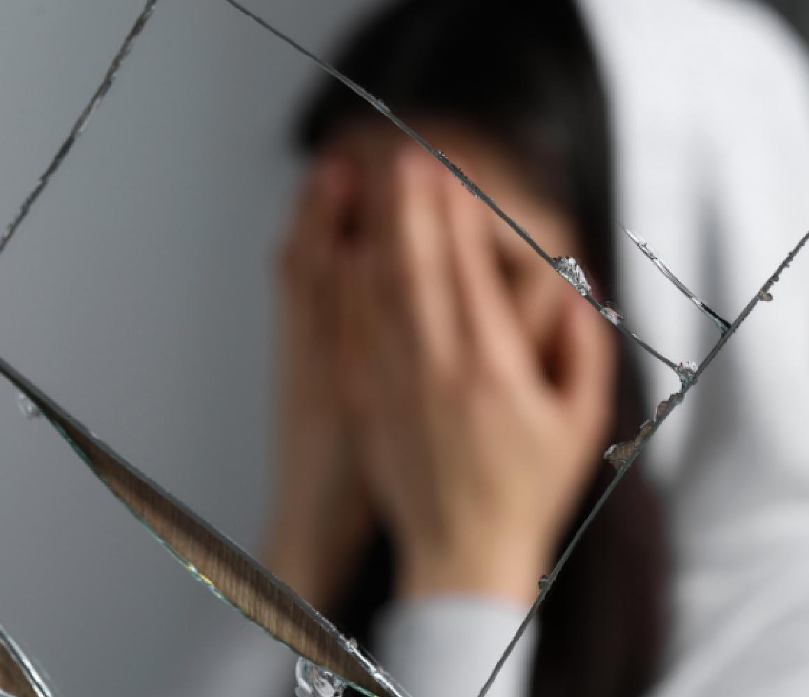 Vrouw met handen voor haar gezicht gezien door gebroken glas