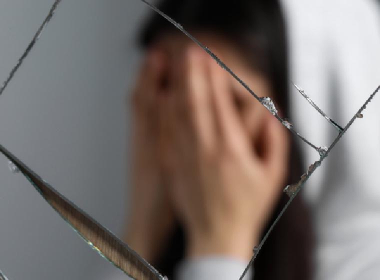 Vrouw met handen voor haar gezicht gezien door gebroken glas