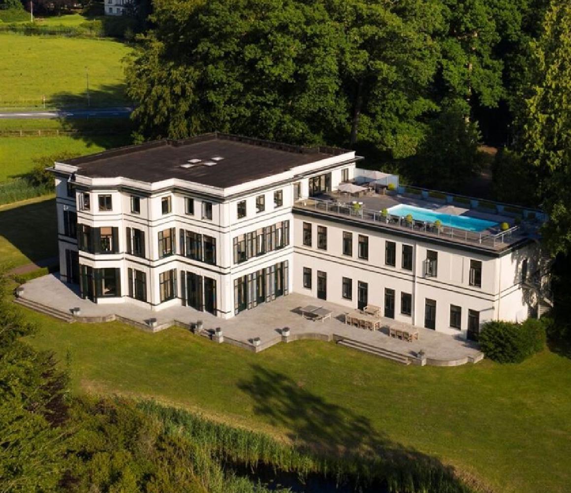 Luchtfoto van een wit landhuis met dakterras en zwembad in het bos