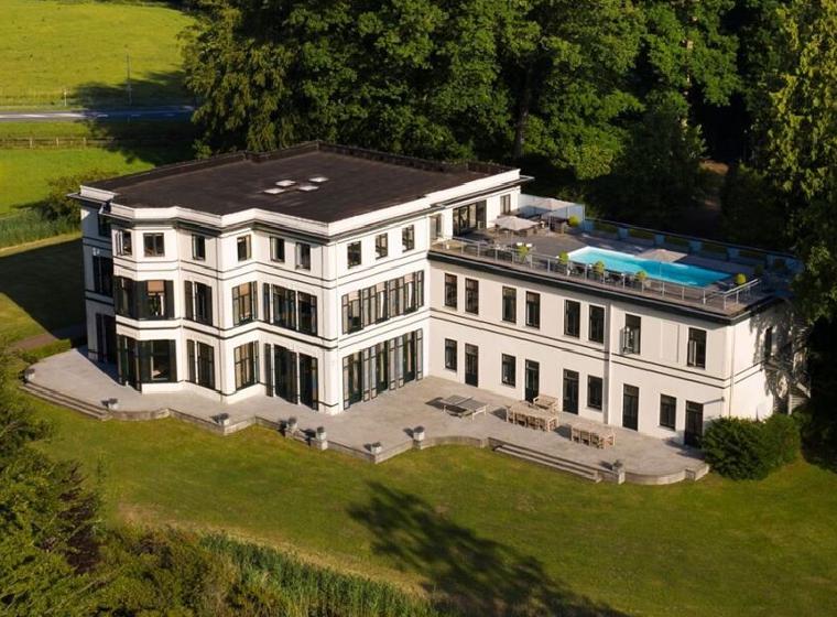 Luchtfoto van een wit landhuis met dakterras en zwembad in het bos