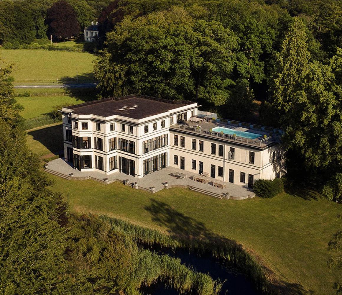 Luchtfoto wit gebouw met pool omgeven door bos en meer