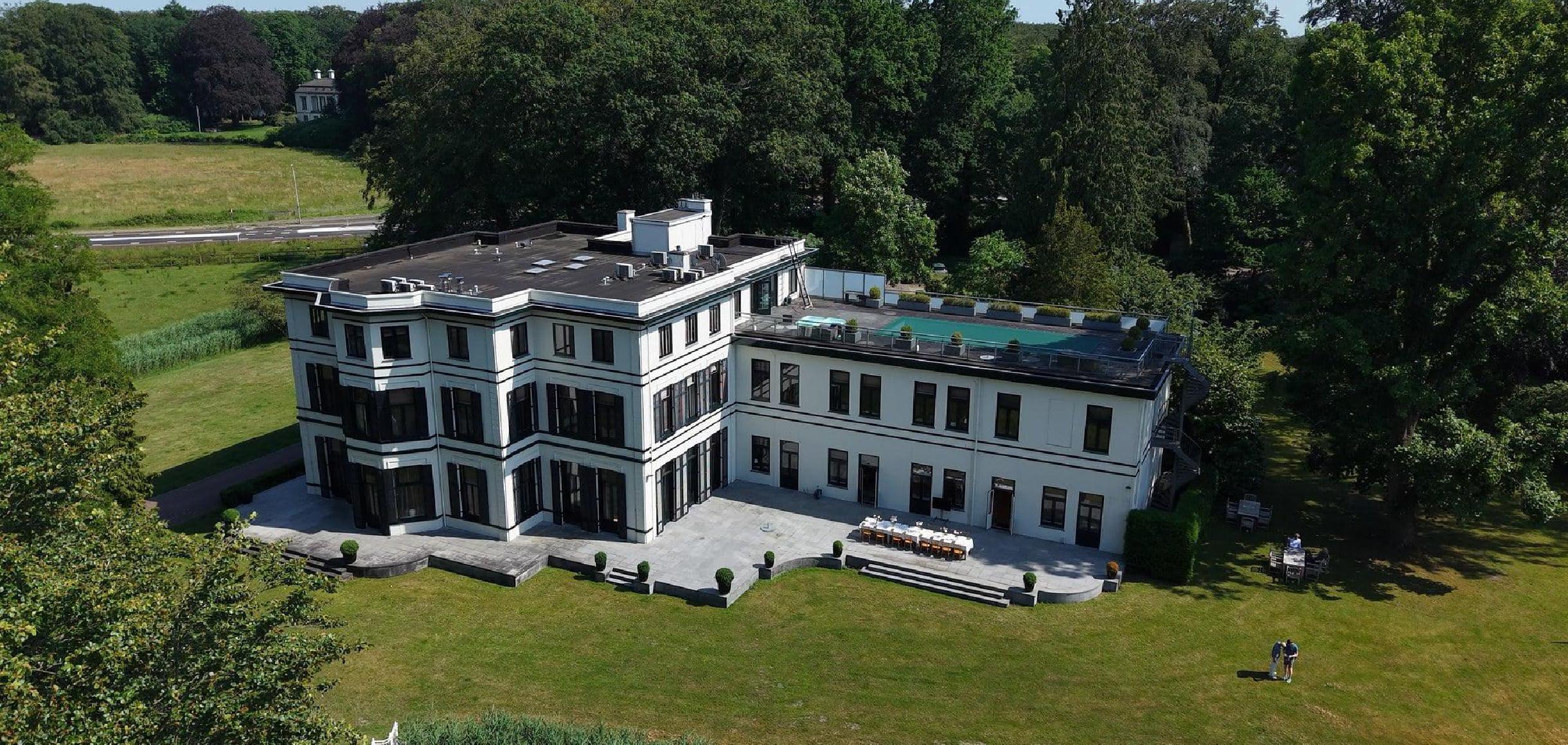 Luchtfoto wit gebouw met pool omgeven door groene weiden