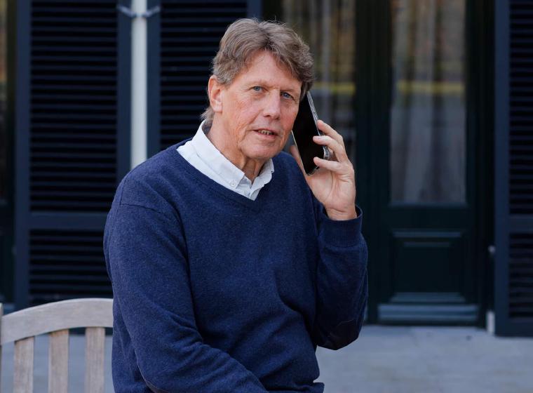 Tjeerd in donkerblauwe trui aan telefoon voor gebouw