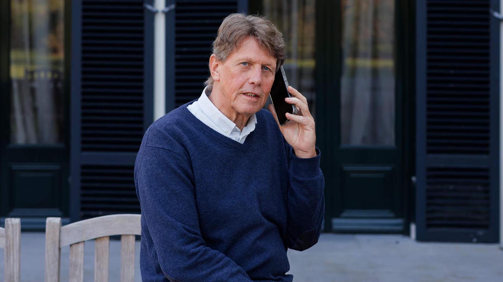 Tjeerd in donkerblauwe trui aan telefoon voor gebouw